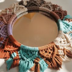 the circular mirror is decorated with multicolored crocheted fringes and tassels