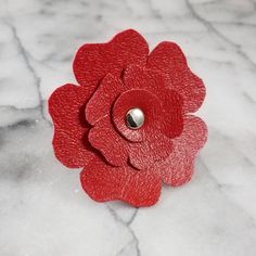 a red flower brooch sitting on top of a white marble surface with a metal button