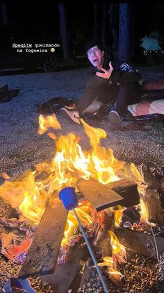 a man sitting in front of a campfire with his hand up to the side