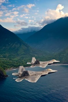 two fighter jets flying over the ocean near mountains