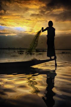 a person standing in the water with a bunch of grass on their hand and sunset behind them