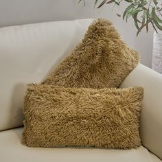 two furry pillows on a white couch next to a potted plant in a living room