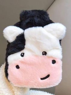 a black and white cow stuffed animal wearing a sweater with its eyes closed, looking at the camera