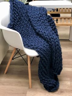 a blue knitted blanket sitting on top of a white chair next to a potted plant