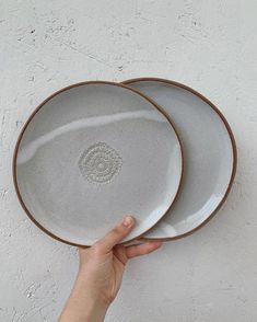 two white plates with brown rims are being held by a person's hand