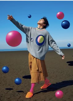 a man standing on top of a sandy beach surrounded by colorful balls in the air