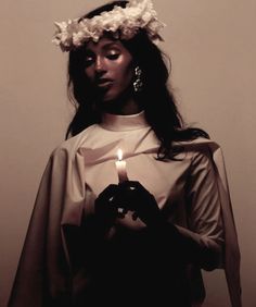 a woman holding a lit candle in her hands and wearing a wreath of flowers on her head