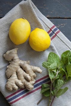 lemons, ginger root and mint on a towel next to two lemons with green leaves