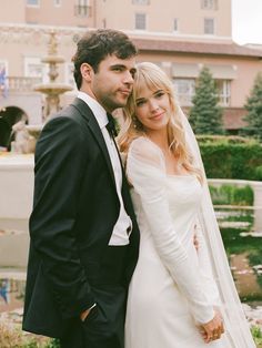 a bride and groom standing next to each other in front of a fountain at their wedding