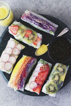 there are many different types of sushi on the plate with sauces and fruit