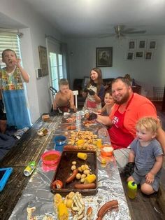 a group of people sitting at a long table with food on it and one person standing in front of the table