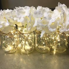 white flowers are in mason jars with fairy lights on them and some string wrapped around the jar