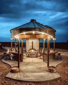 an outdoor gazebo with lights on the top and chairs around it in front of a cloudy sky