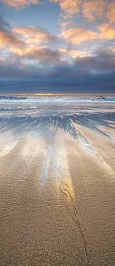 the beach is covered in sand and water under a colorful sky with clouds above it