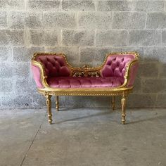 a pink and gold couch sitting in front of a brick wall on concrete flooring