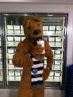 a man dressed in a bear costume holding a coffee cup while standing next to a refrigerator