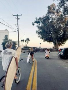 two people riding bikes with surfboards on the back of their backs as they ride down the street