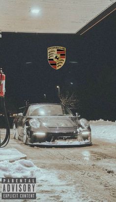 a car is parked in the snow next to a gas pump and an emblem on the wall