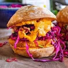 a sandwich with meat, cheese and coleslaw is on a wooden table next to other food items