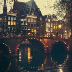 a bridge that is over some water with buildings in the background and lights on it