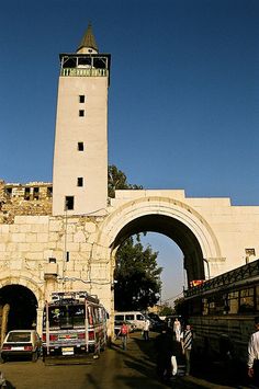 people walking around in front of an arch with a clock tower on the other side