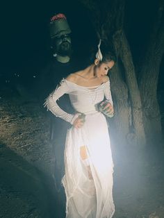 a woman in a white dress standing next to a tree