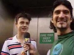 two men standing next to each other in front of an elevator holding microphones and talking