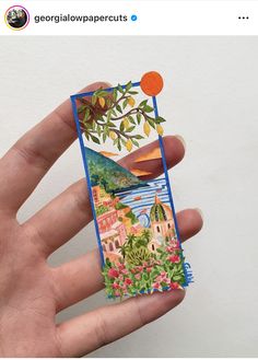 a hand holding up a small card with an image of a tree and buildings on it