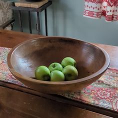 a wooden bowl filled with green apples on top of a table