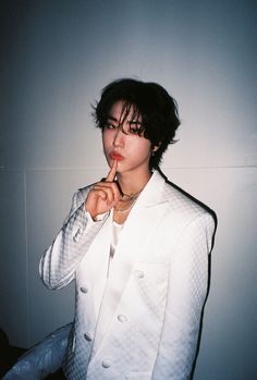 a person in a white suit posing with their finger on her lips and looking at the camera