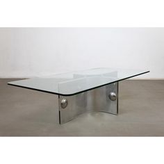 a glass and chrome coffee table with two balls on the bottom, in front of a white wall