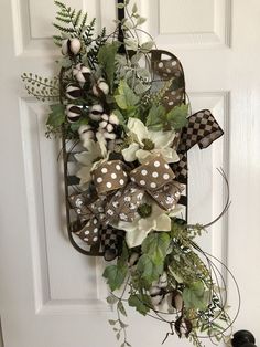 a wreath hanging on the front door of a house with white flowers and green leaves