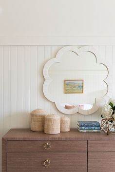 a white cloud shaped mirror on top of a dresser next to a vase with flowers