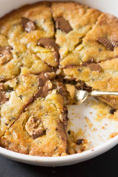 a chocolate chip cookie in a white bowl with a serving spoon on the side and one slice missing