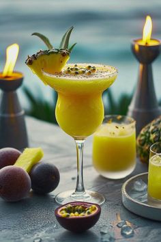 two glasses filled with drinks sitting on top of a table next to fruit and candles