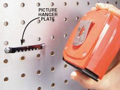 a person is holding an orange object in front of a metal pegboard with holes on it