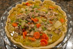 a pie with meat and vegetables in it on top of a glass plate sitting on a table