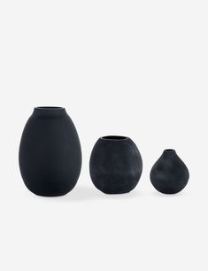 three black vases sitting next to each other on a white surface with no one around them