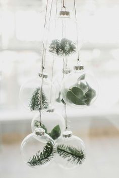 christmas ornaments hanging from the ceiling in front of a window with greenery on them