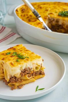 a white plate topped with lasagna next to a casserole dish filled with meat and cheese