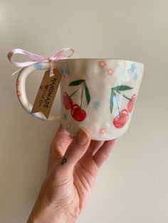 a hand holding a cup with cherries on it and a ribbon around the handle