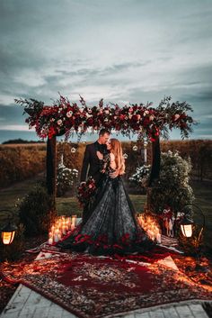 a man and woman are standing under an arch with flowers on it, surrounded by candles