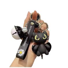 a hand holding a black cat keychain with an egg in the shape of a spider