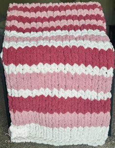 a pink and white crocheted blanket sitting on top of a table