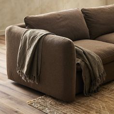 a brown couch sitting on top of a wooden floor next to a rug and wall