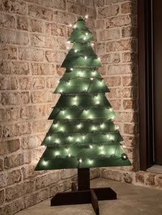 a lighted christmas tree on a stand in front of a brick wall