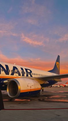 a large jetliner sitting on top of an airport tarmac at sunset with the sky in the background