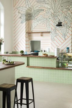 a green tiled kitchen with stools in front of the counter and an art work on the wall