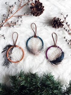 three small hoop earrings with feathers and beads hanging from them on a white fur surface