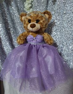 a teddy bear wearing a purple dress sitting on top of a chair with sequins